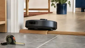 Robotstøvsuger der krydser et trædørtrin med en lav rampe og målebånd ved siden af